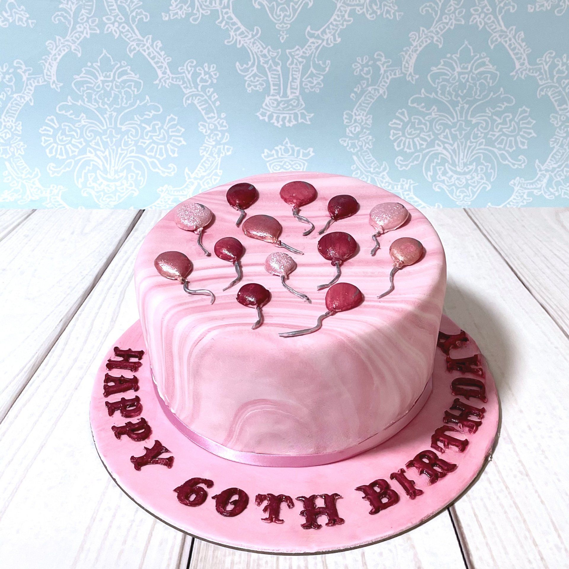 60th Birthday cake with marbled pink fondant and assorted pink fondant balloons.