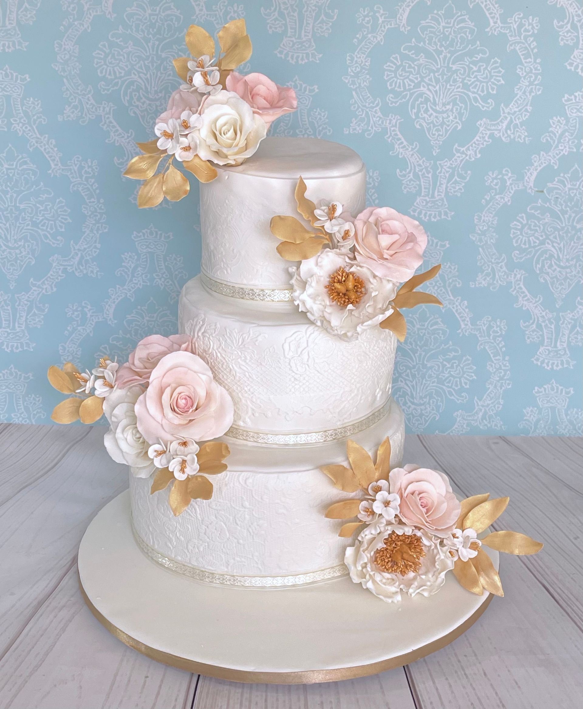 3 tier Wedding Cake Sails Resort Port Macquarie. White embossed fondant tiers, Trimmed with Ribbon and Decorated with Handmade Sugar Flowers, Sugar leaves in white, Champagne gold and soft pink