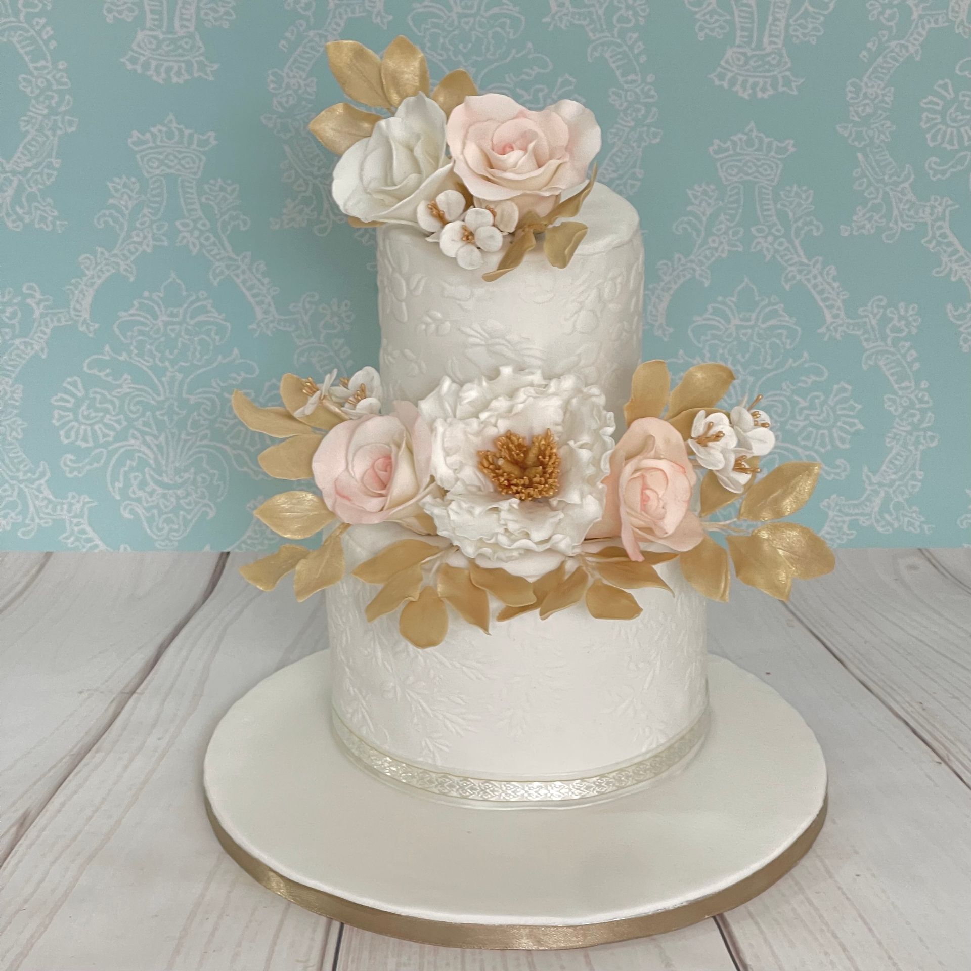 2 tier Wedding Cake Sails Resort Port Macquarie. White embossed fondant tiers, Trimmed with Ribbon and Decorated with Handmade Sugar Flowers, Sugar leaves in white, Champagne gold and soft pink