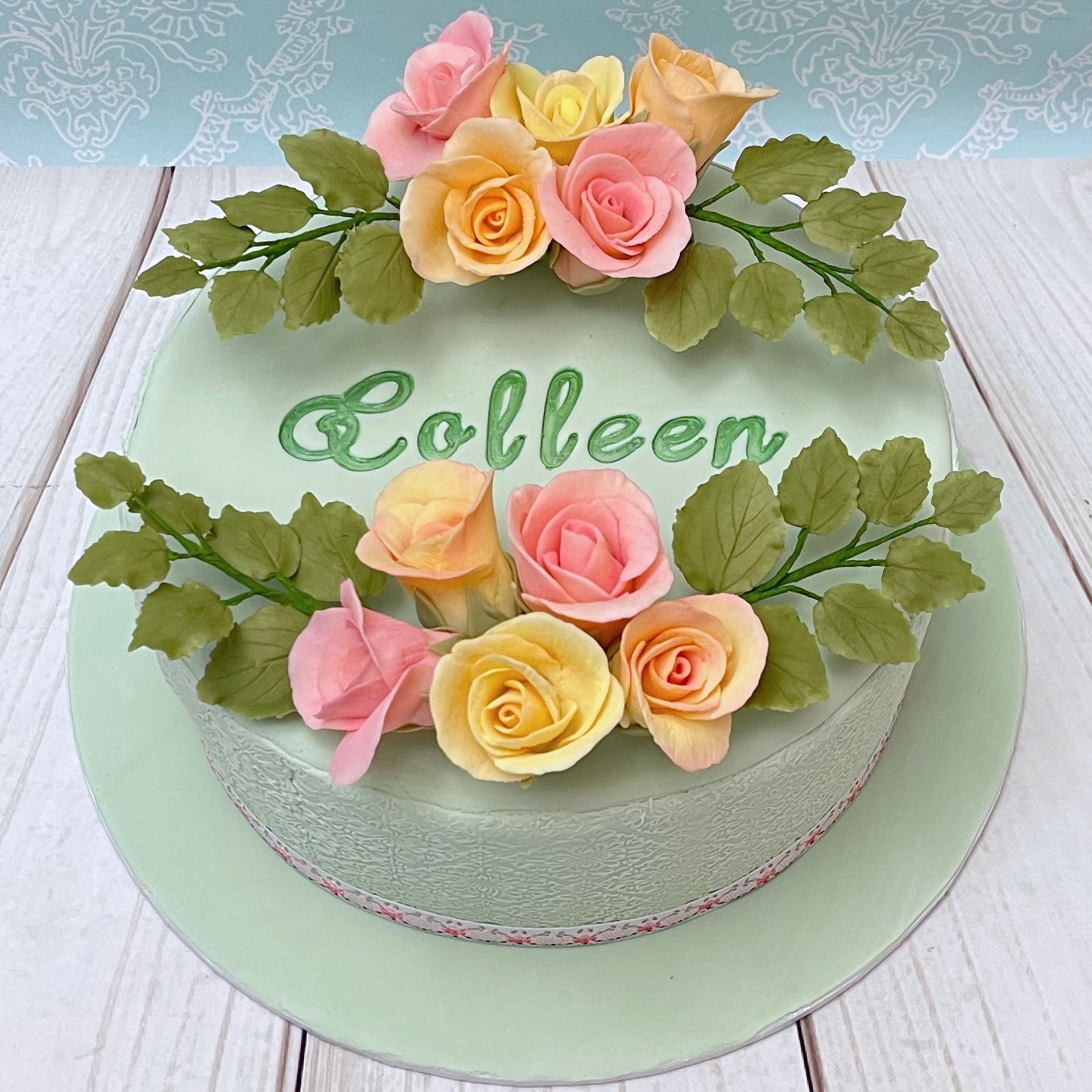 Soft Green Fondant Birthday Cake With Pastel Pink, Apricot and Lemon Sugar Roses and Sugar Leaves. Embossed sides and Hand Painted Personalised name in the centre.