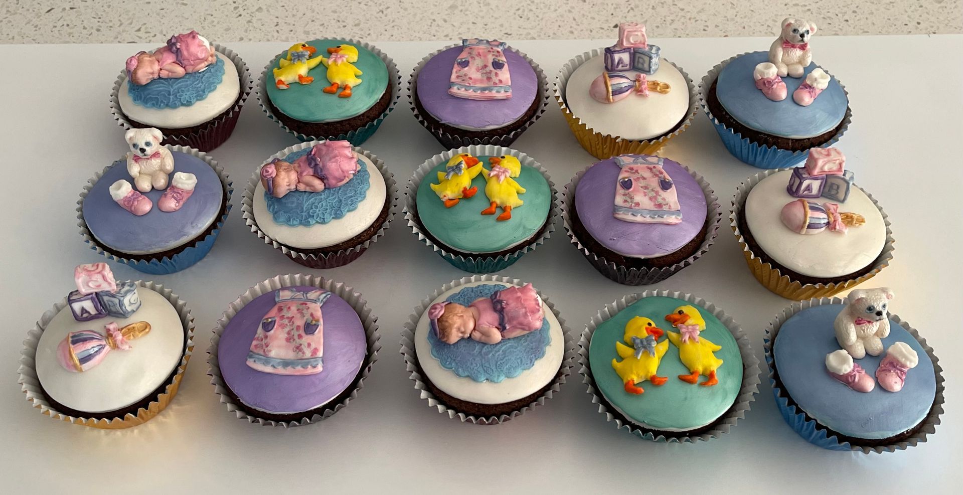 Cute Baby Girl Themed Cupcakes. Some with Fondant Baby Girl toppers, some with Fondant Dress toppers, some with fondant bear and bootie toppers, some with rattle and blocks topper and some with cute little ducks topper. Fondant