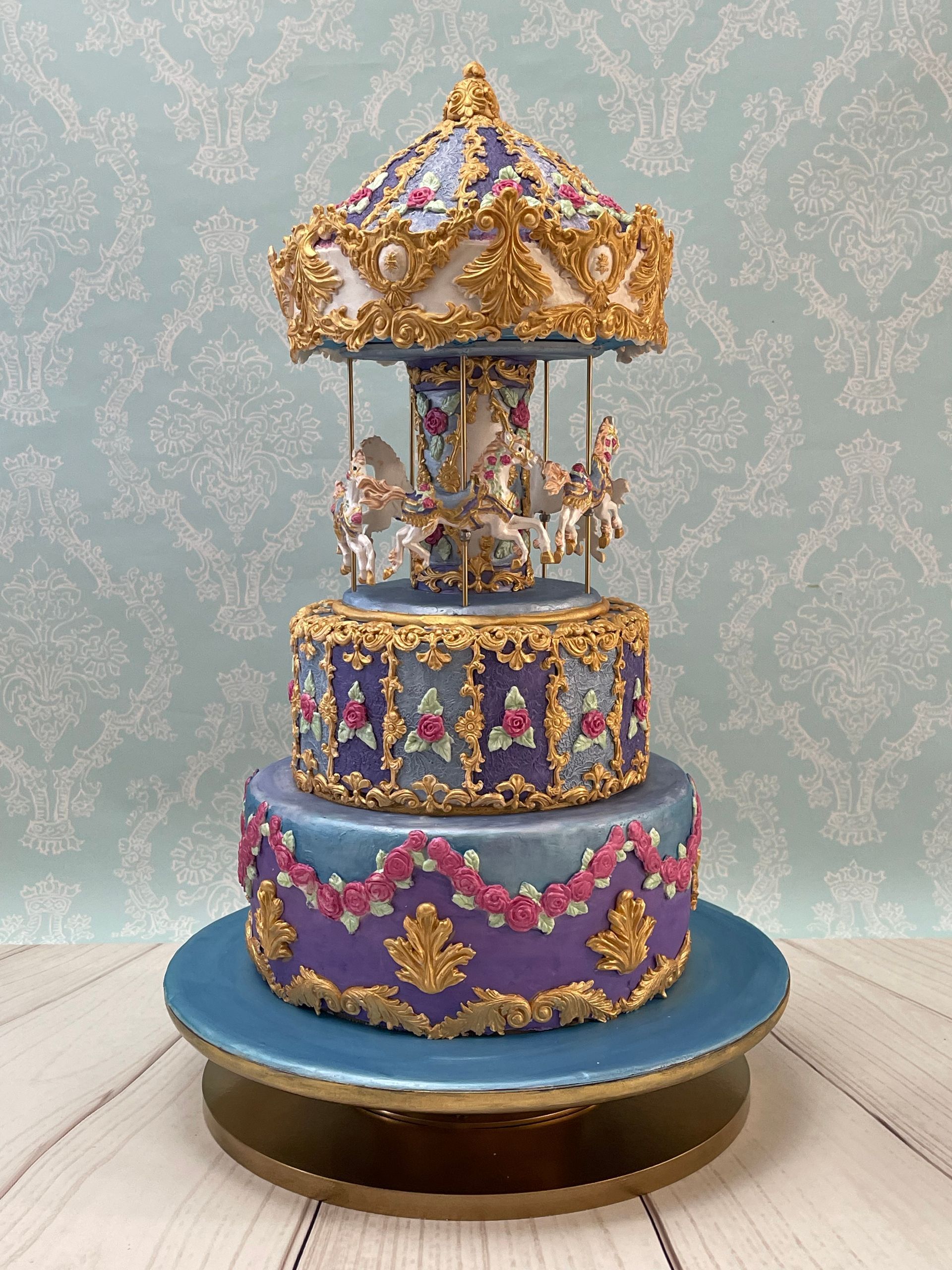 Tiered Baby Girl Carousel Cake. With ornate gold fondant mouldings, Fondant Roses and Fondant carousel horses.