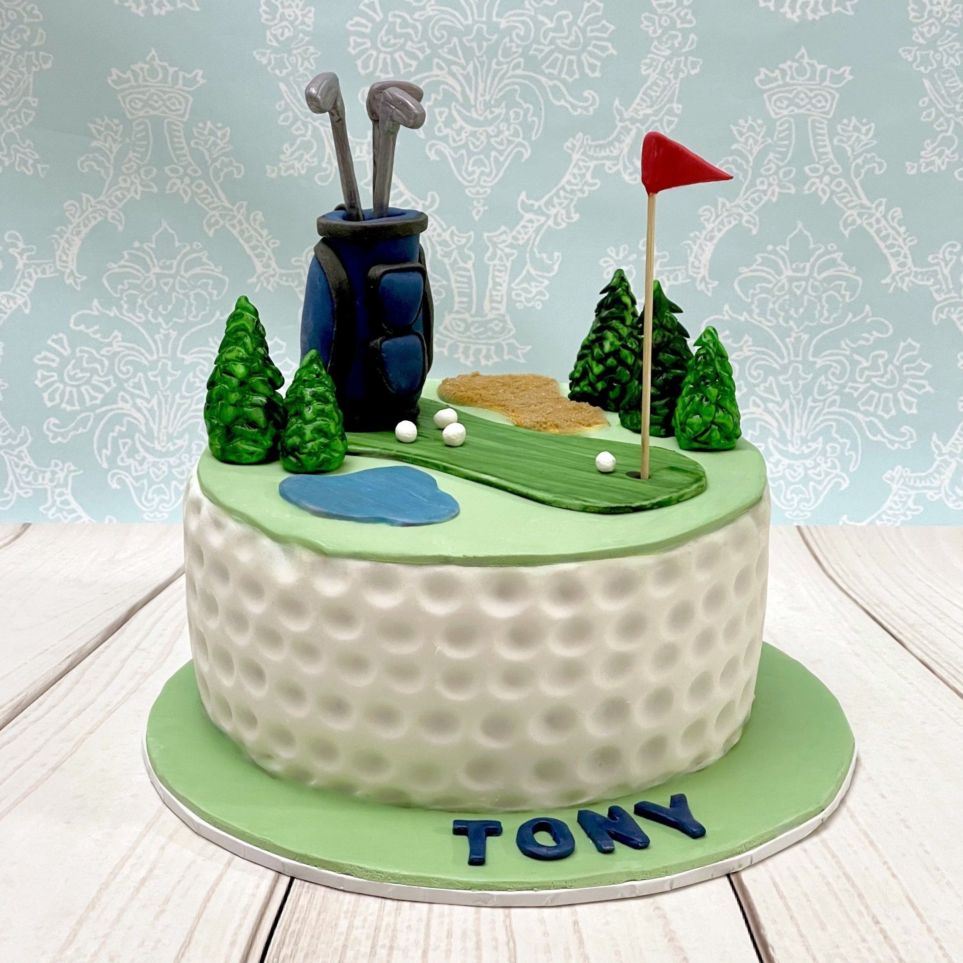 Golf Themed Birthday Cake with fondant trees, Fondant golf Bag, Fondant golf clubs, Fondant gold balls, Fondant putting green and a fondant gold ball texture around the sides.