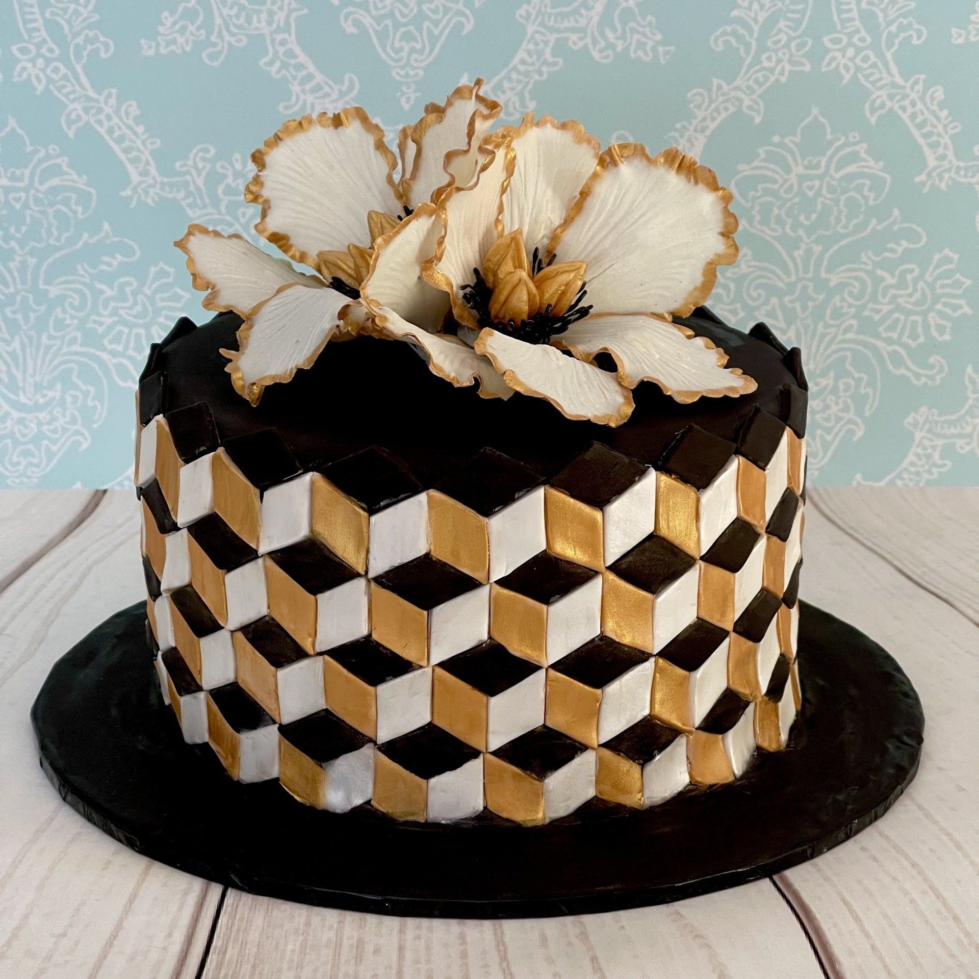 Sylish Black, gold and white cake with Fantsy sugar flowers on top and an optical illusions box effect around the sides.