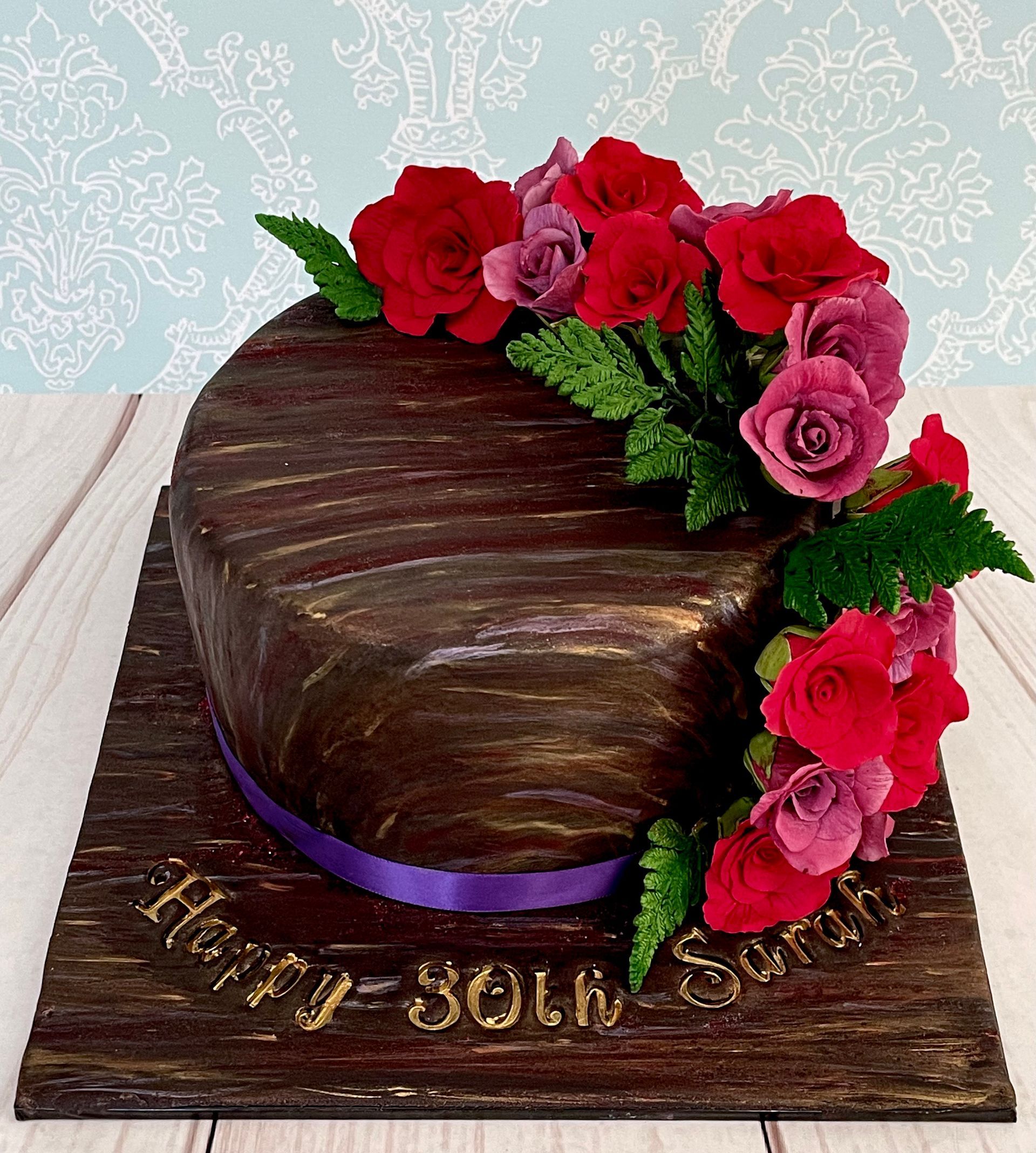 30th Birthday Cake. Marbled fondant in rich metallic chocolate, gold, and mauve tones, with a spray of red and mauve sugar roses and sugar fern leaves cascading down one side, purple ribbon and hand painted gold birthday sentiments.