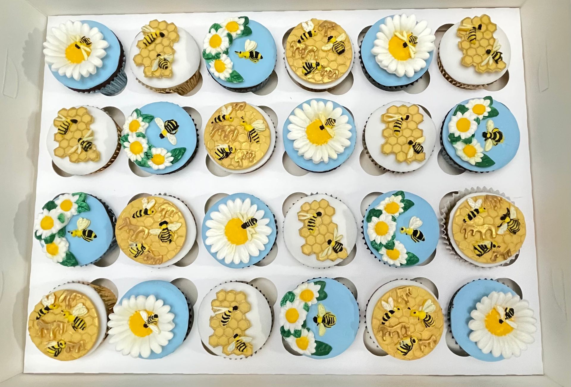 Cupcakes in a white soft blue and gold theme decorated with fondant daisies fondant honeycomb and fondant honey bees.