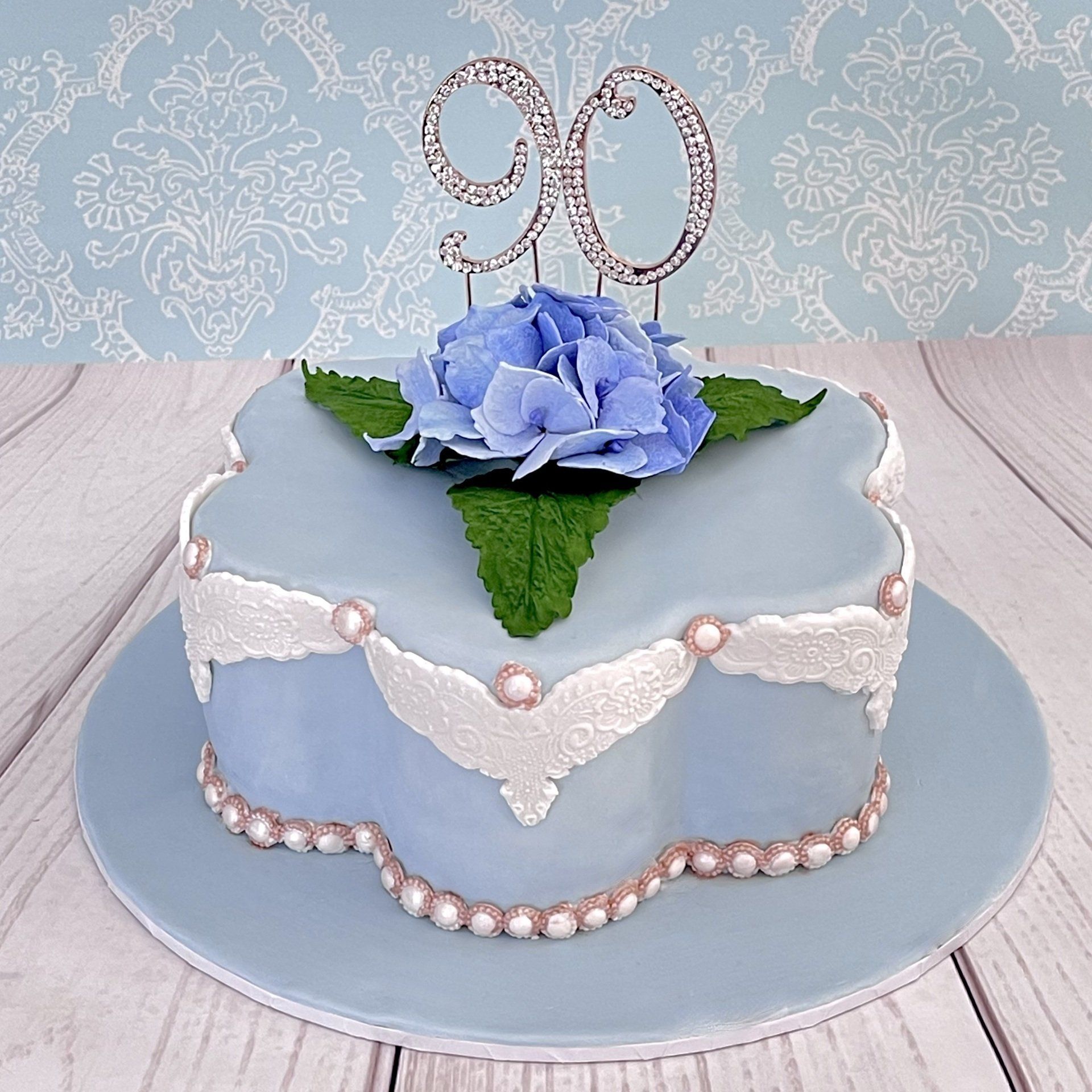 Pretty soft blue 90th birthday cake with hand made sugar hydrangeas sugar lace sugar pears and a rose gold diamante 90.
