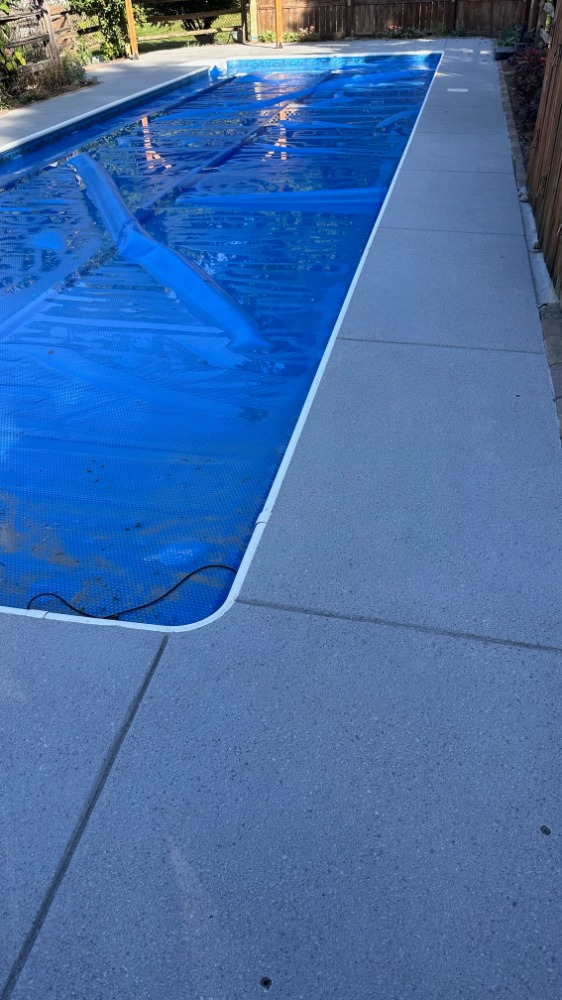 A swimming pool with a blue cover on it and a concrete patio.
