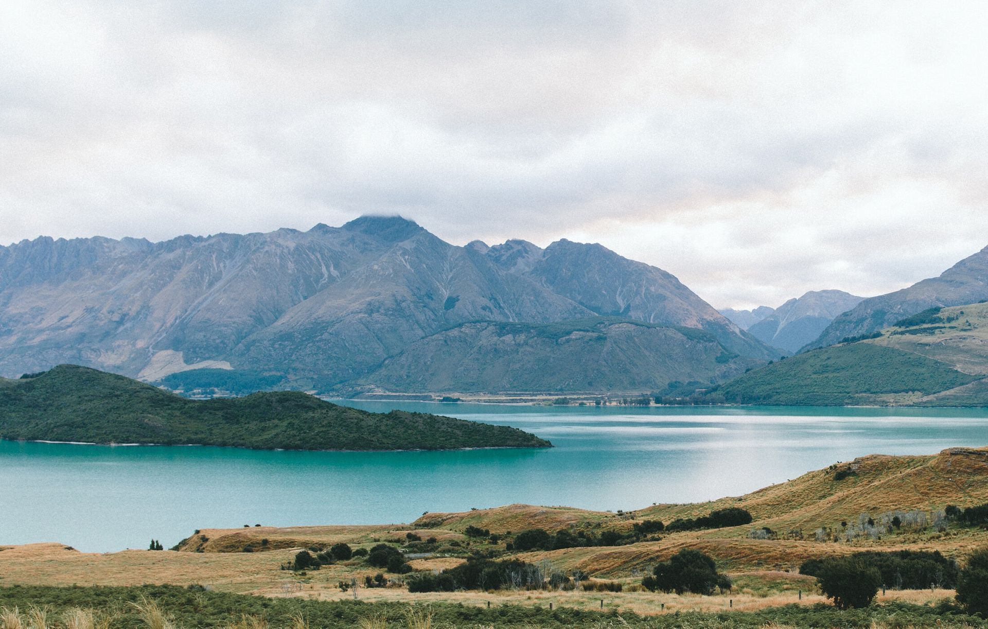 Lake and mountains under a cloudy sky. Turquoise water and brown hills in the foreground.
