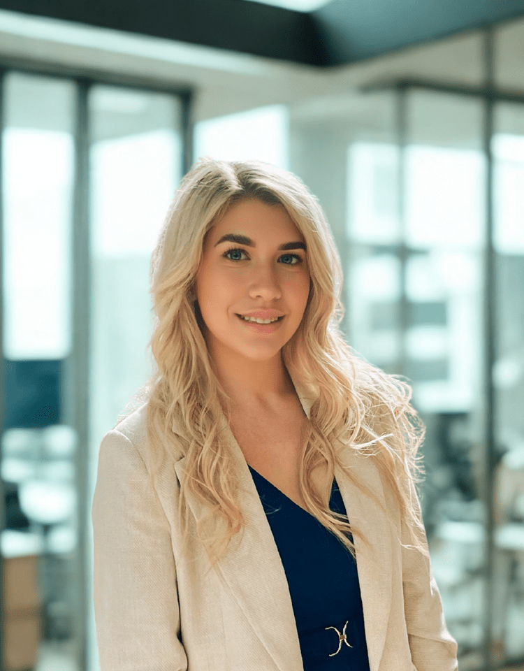 Woman with blonde hair wearing a cream blazer and navy top, smiling in an office setting.