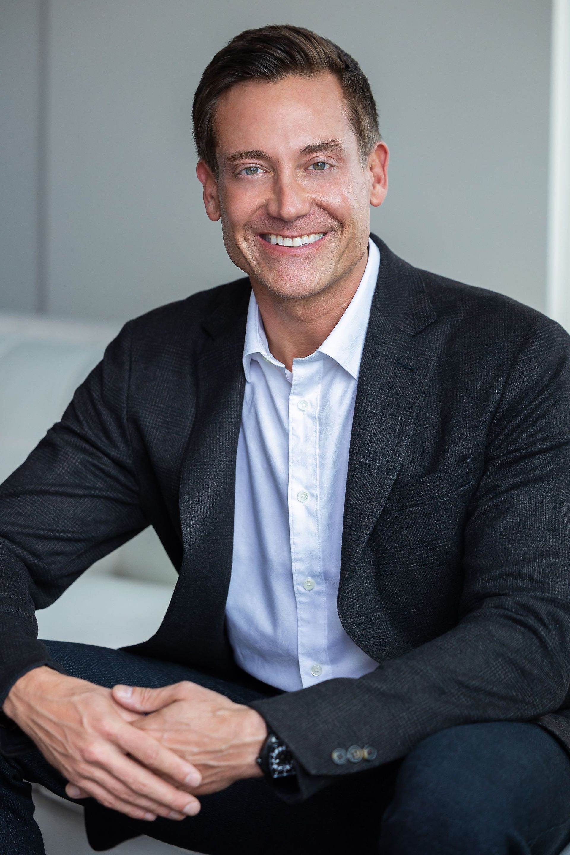 Man in blazer and open-collared shirt smiles while seated against a white background.