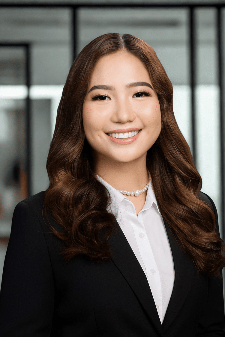 Woman in a black suit smiles, wearing a pearl necklace, white shirt, and long brown hair; professional setting.