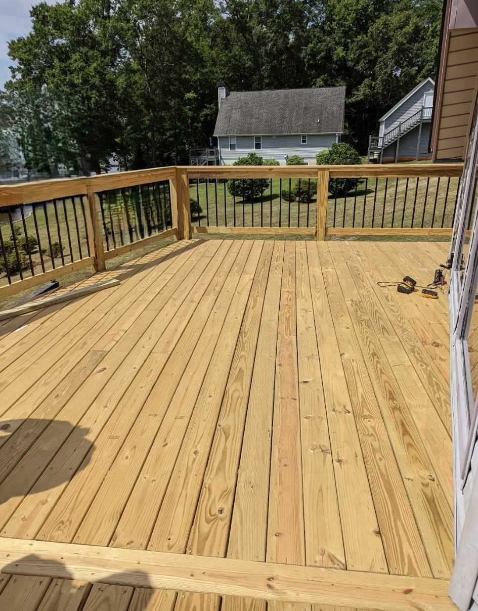 Wooden deck with black railing overlooking a yard and house.