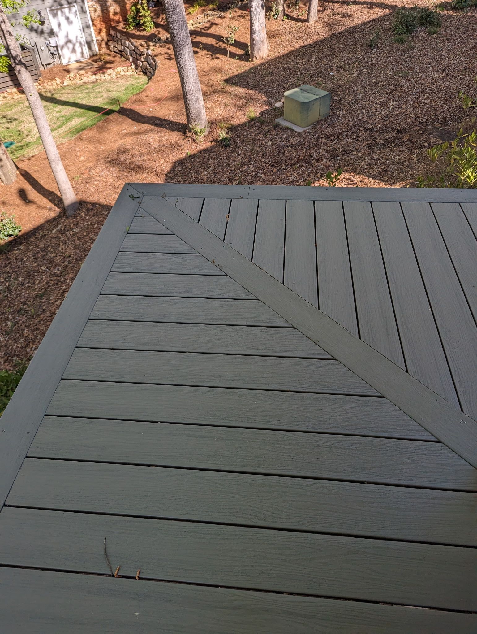 A top-down view of a dark gray wooden deck with triangular design, leading into a shaded brown area.