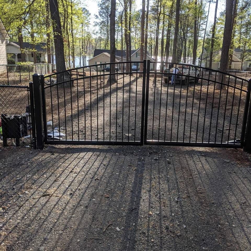 A wrought iron gate surrounds a gravel driveway with trees in the background