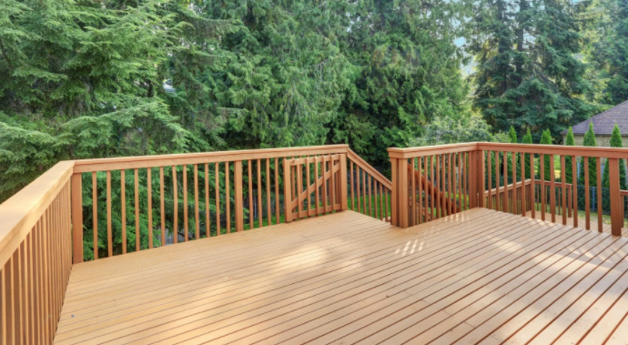 An empty wooden deck with a railing and trees in the background.