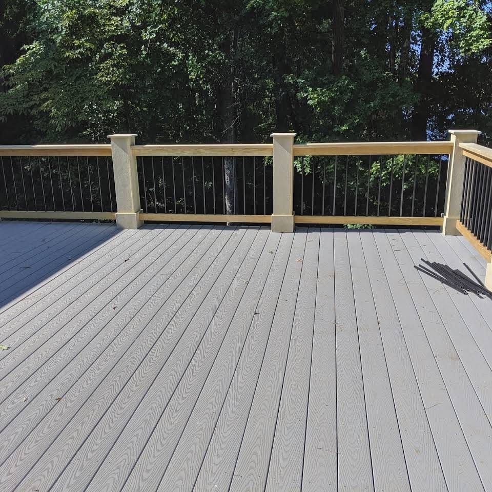 A gray deck with a wooden railing and trees in the background