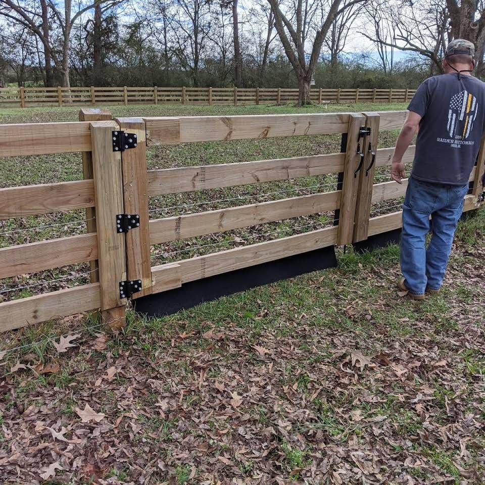 A man standing next to a wooden fence in a field