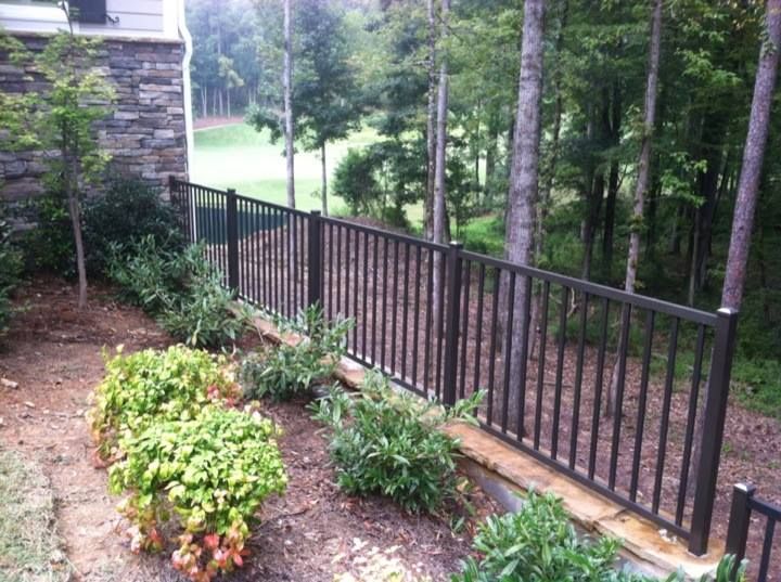 A black fence surrounds a garden with trees in the background