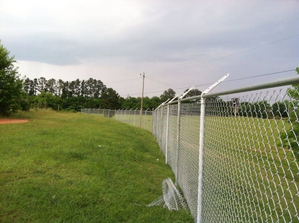 A chain link fence surrounds a grassy field with trees in the background