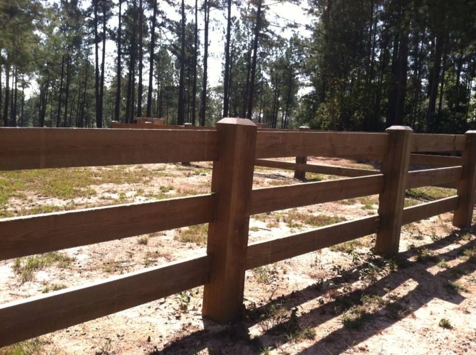 A wooden fence surrounds a field with trees in the background