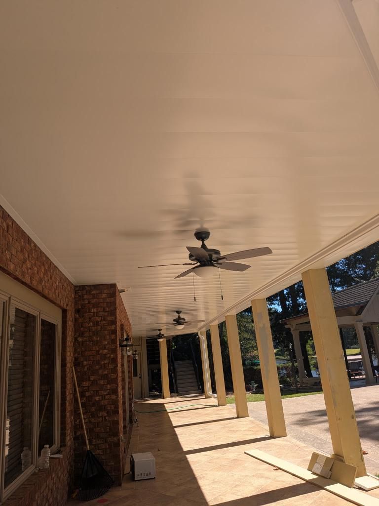 Covered outdoor patio with white ceiling, brick wall, and beige columns; two ceiling fans.