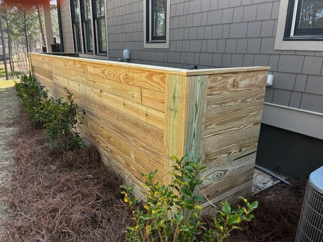 Wooden fence against a house with bushes and brown mulch.