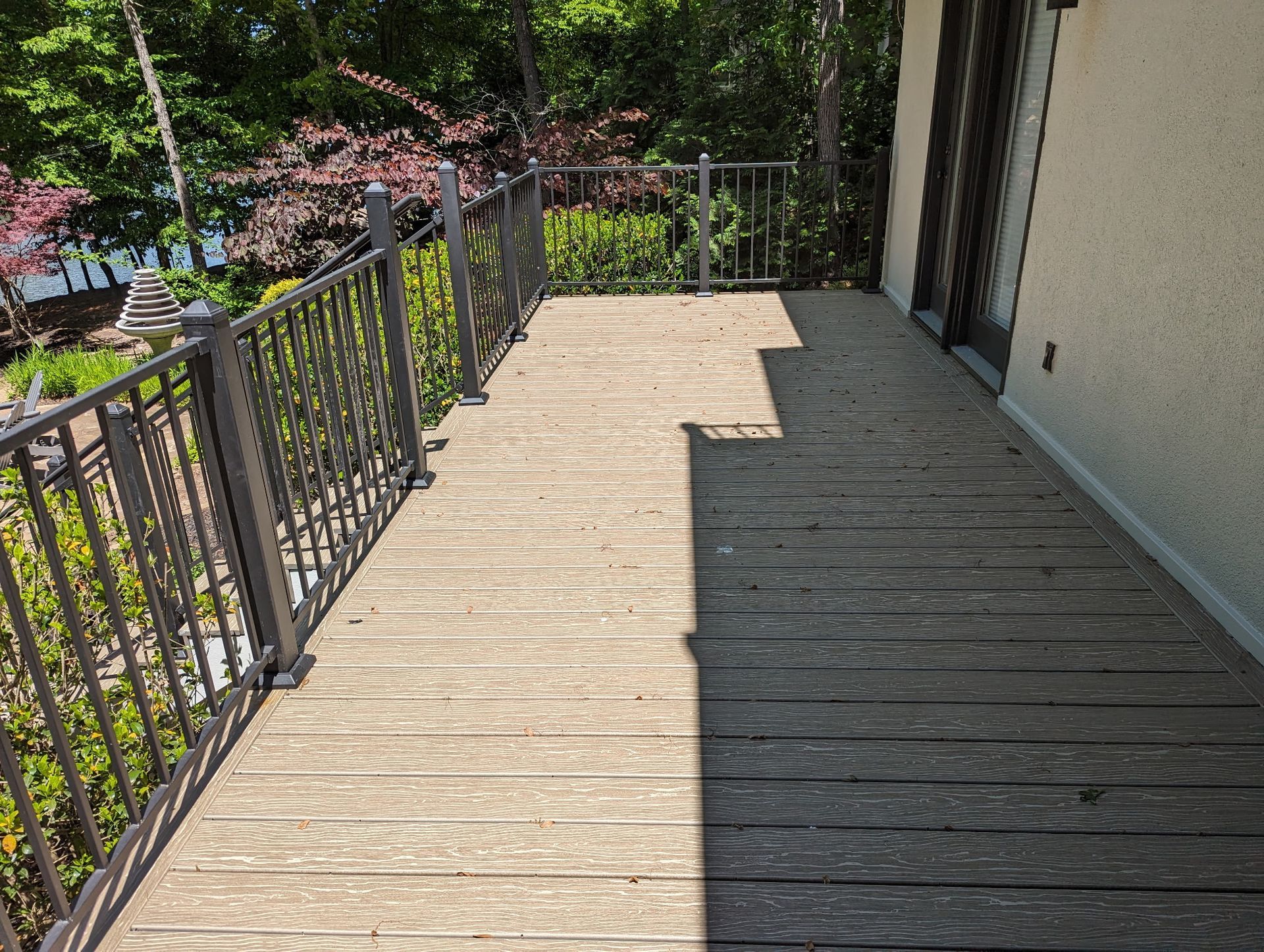 Wooden deck with metal railing next to a building, partially in the sun.