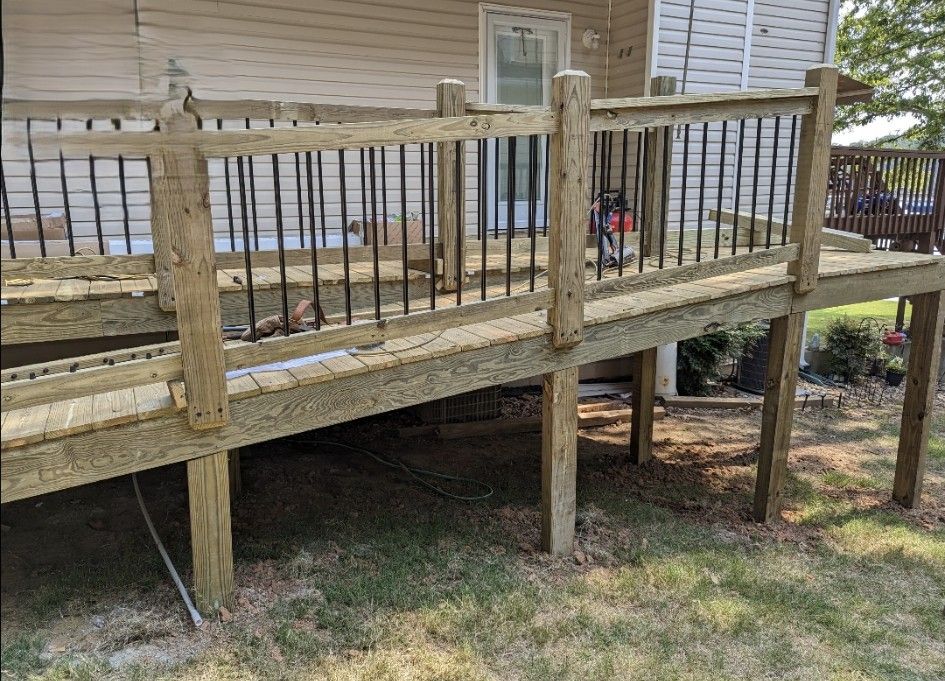 Wooden deck with a ramp and black railings, surrounded by grass.