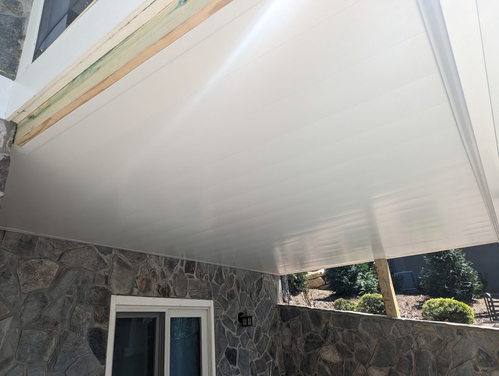 White ceiling of a patio, attached to a stone wall. Sunlight illuminates the area.