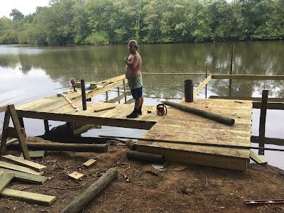 A man is standing on a wooden dock next to a lake.
