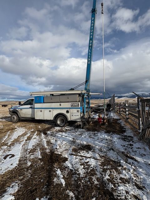 Truck-mounted well drilling rig on snowy ground near a fence. Sky is cloudy.