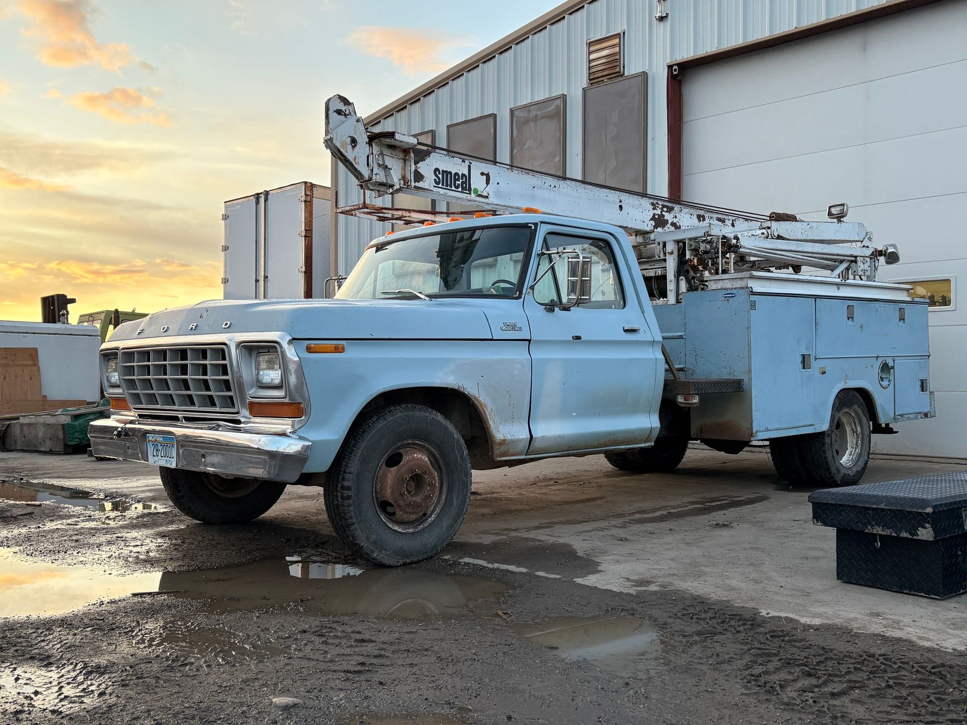 Light blue Ford bucket truck parked near a building, with the boom extended.