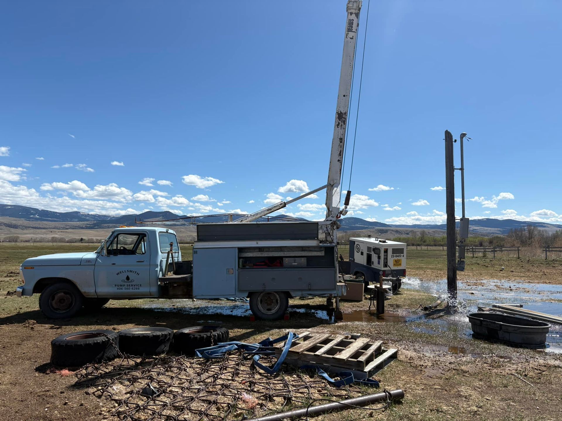 Well drilling truck in a field on a sunny day. Equipment and water present.