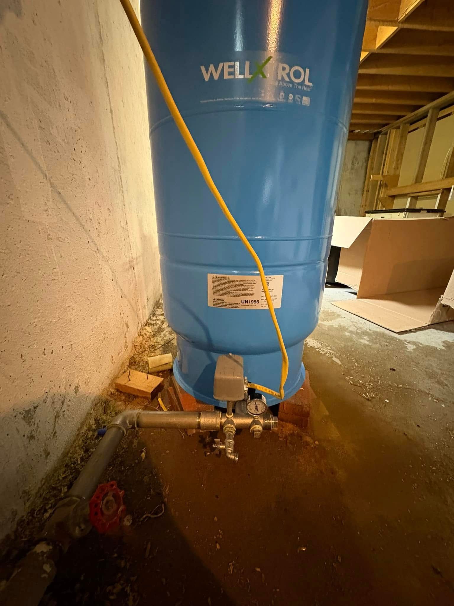 Blue Well-X-Trol water pressure tank in a basement with yellow electrical wire and plumbing.