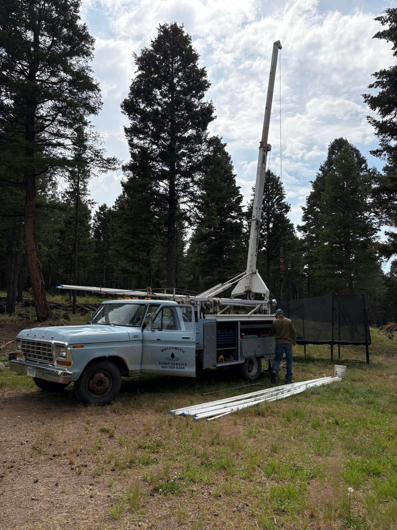 Blue truck with a drilling rig in a forest, person near it.