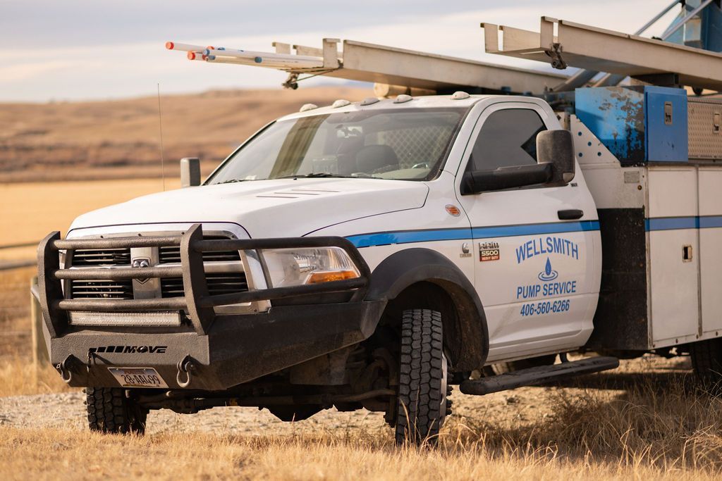 White truck with drilling equipment in a field, under a blue sky.