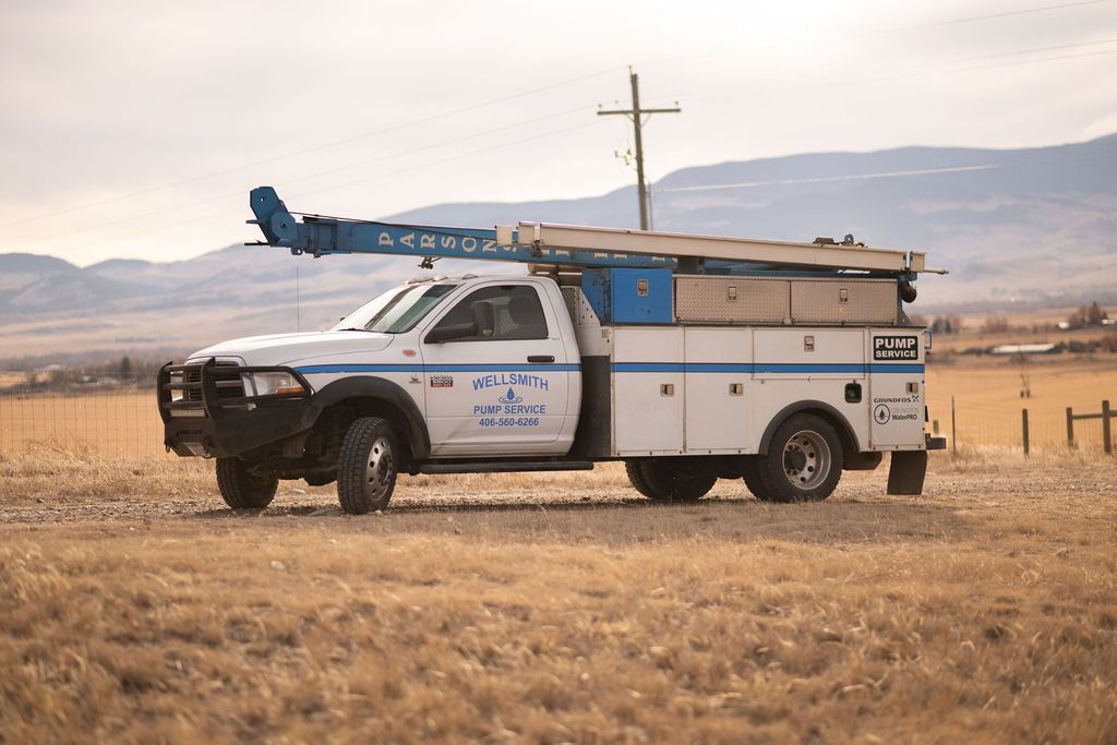 White utility truck with a crane parked on a grassy field with mountains in the background.