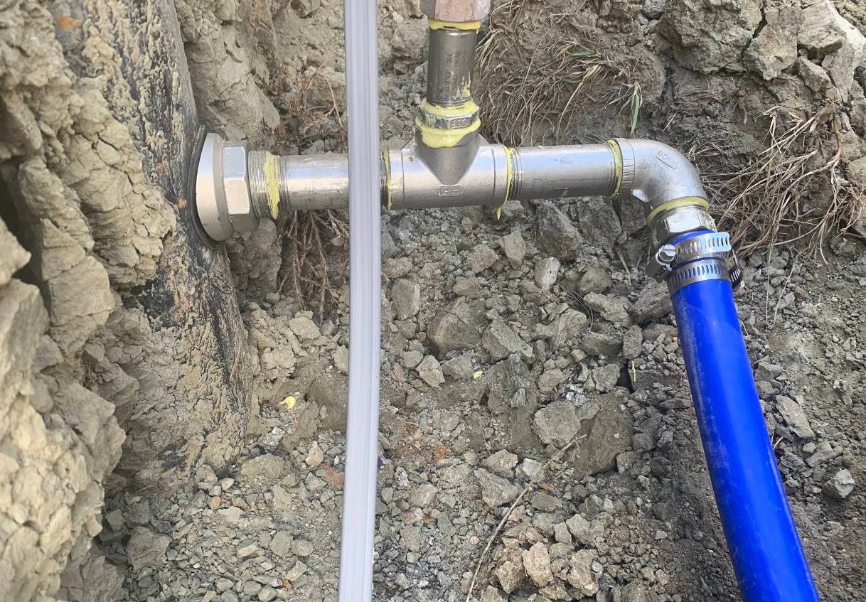 Metal pipe fittings attached to a wall, with a blue hose connected, water flowing.