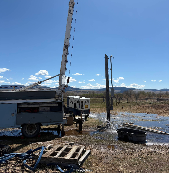 Well drilling rig at work in a field on a sunny day with blue sky. Water spraying.