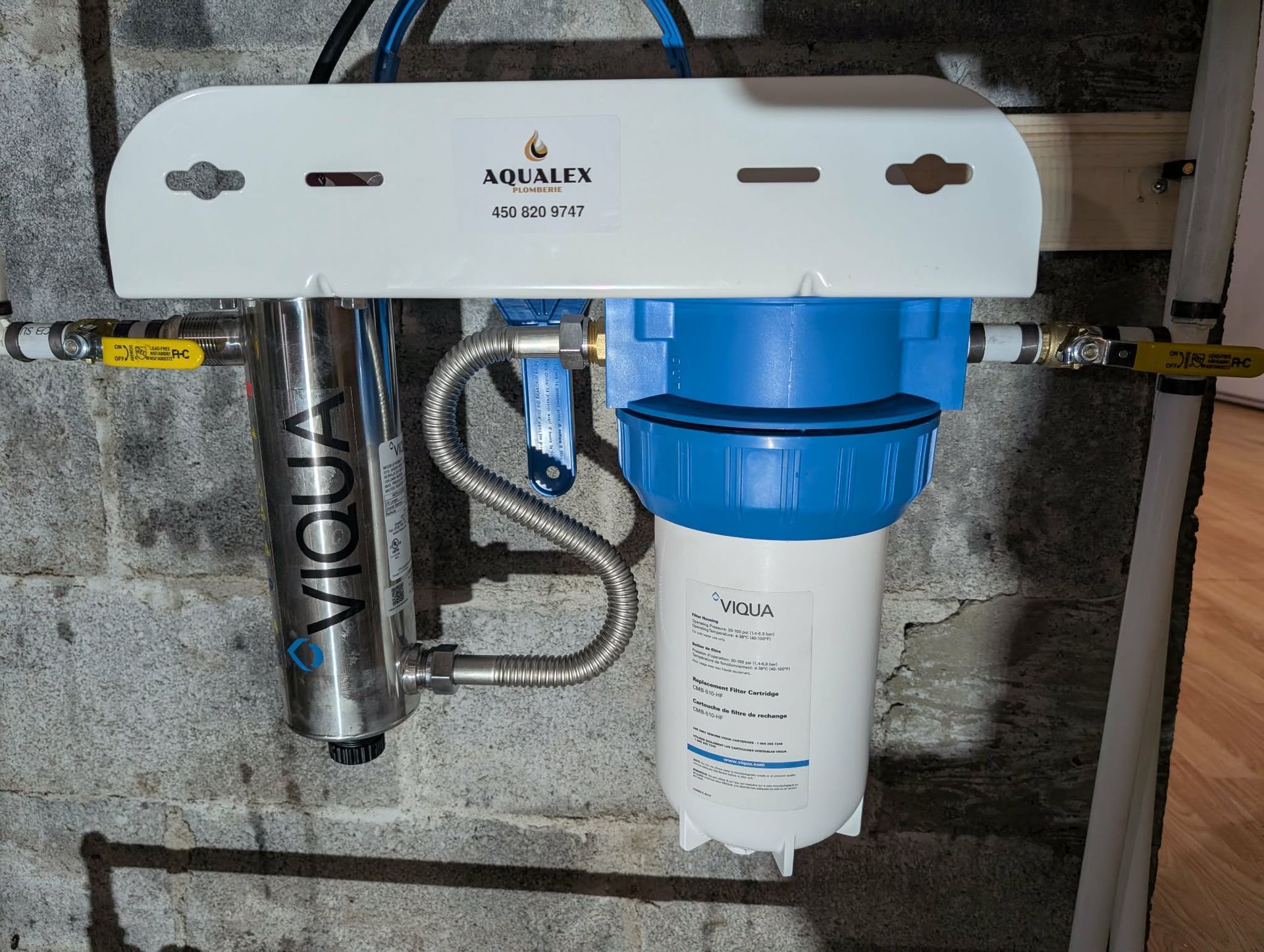 Système de filtration d'eau fixé sur un mur en béton. Comprend un filtre UV, un filtre à sédiments et un support de fixation blanc.