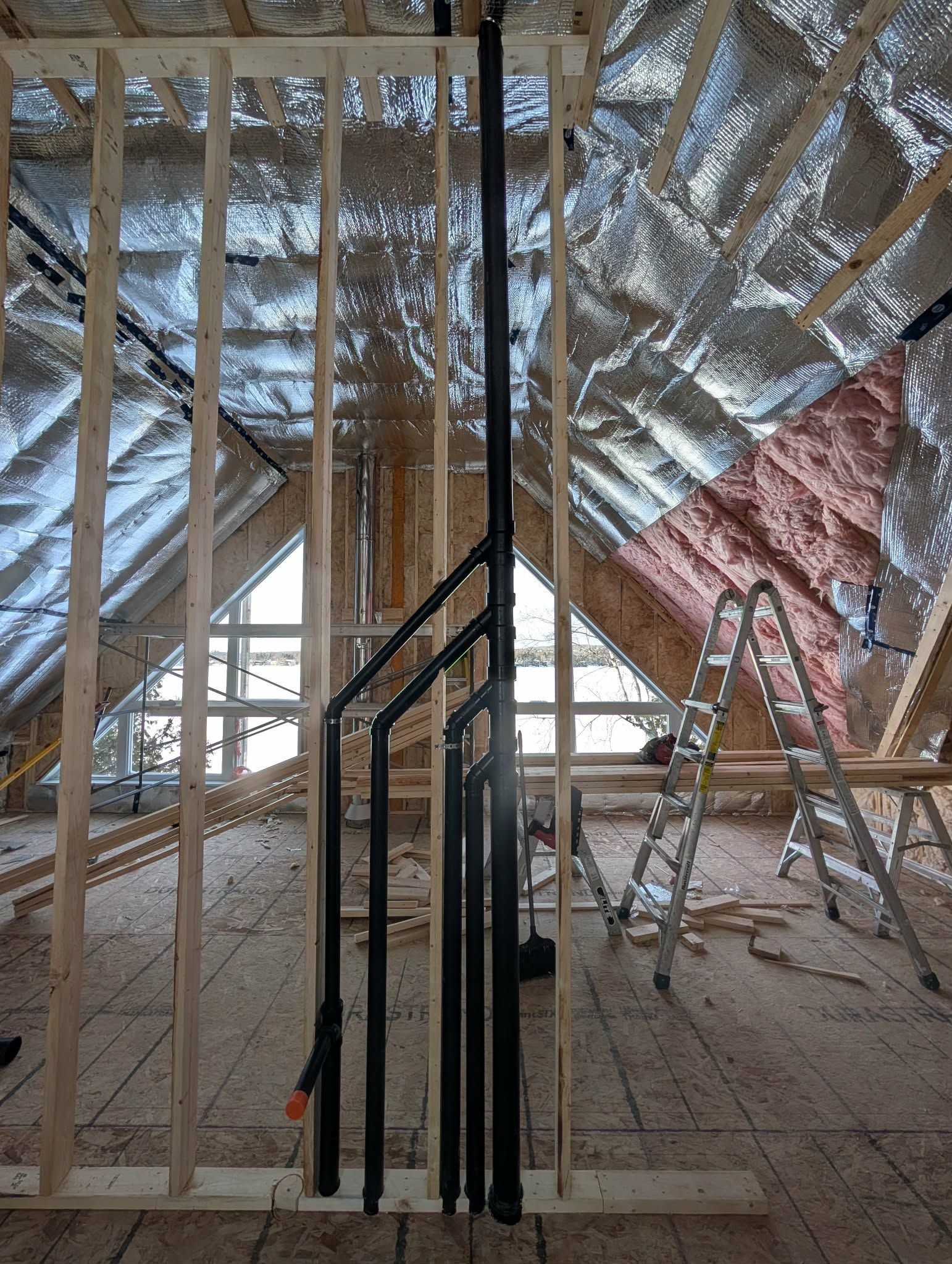 Intérieur d'un chantier de construction avec charpente en bois apparente et tuyaux noirs verticaux.