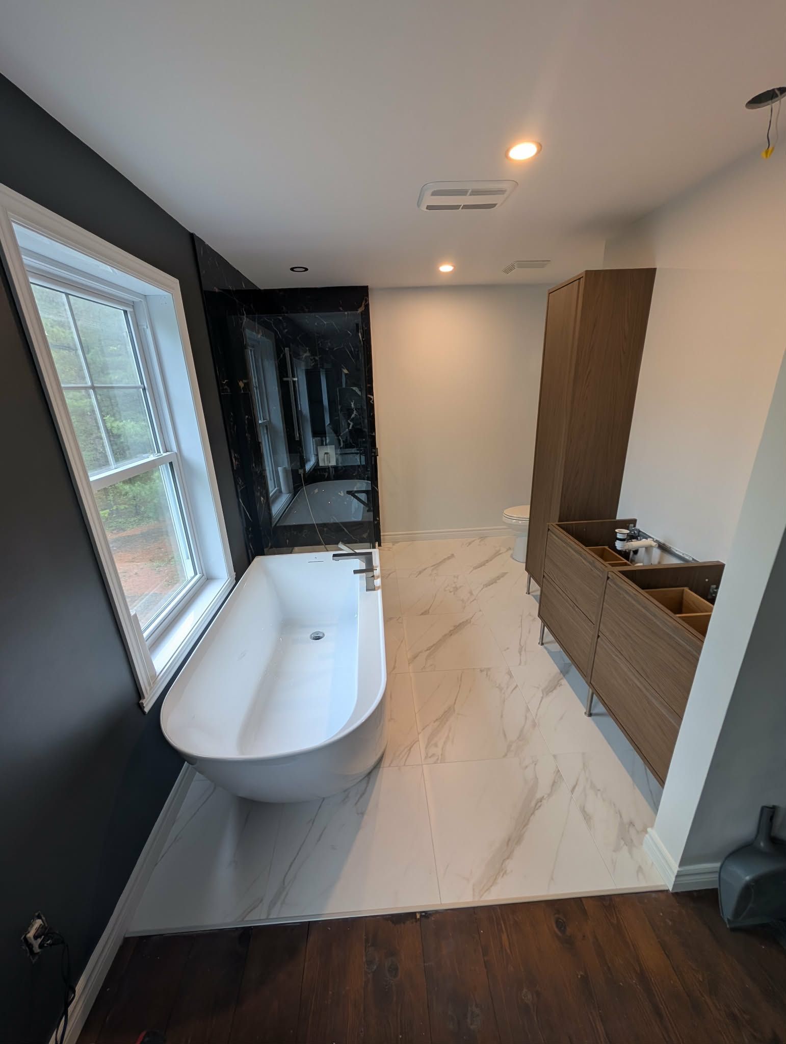 Salle de bains avec baignoire blanche, mur d'accent gris foncé et meuble-lavabo en bois.