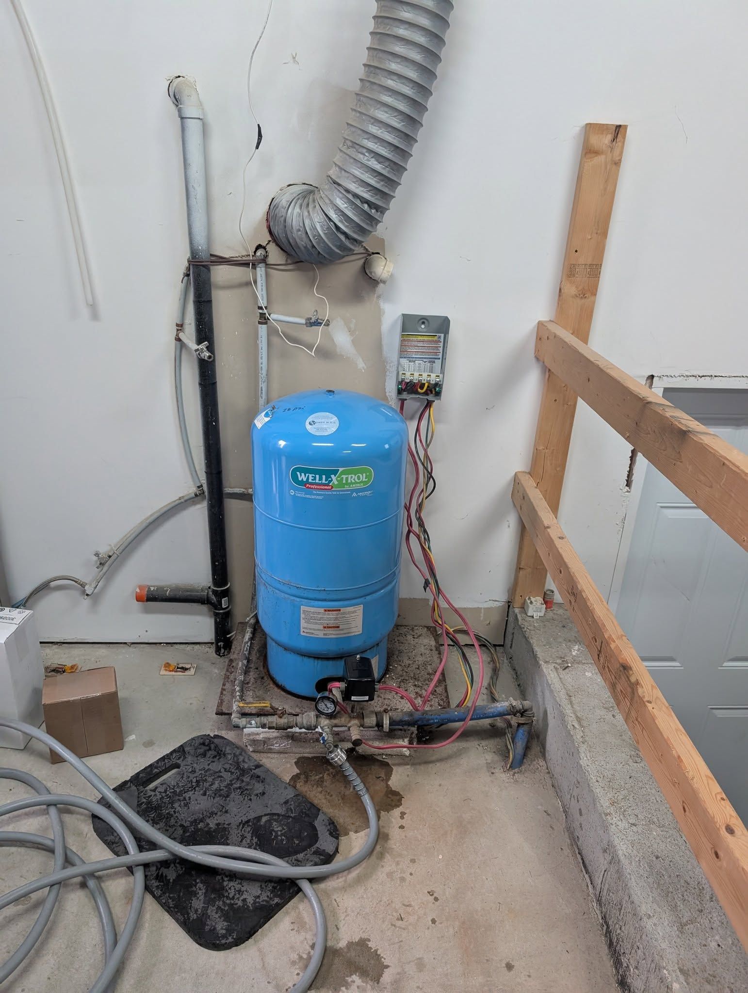 Réservoir d'eau sous pression bleu avec plomberie dans un coin du garage.