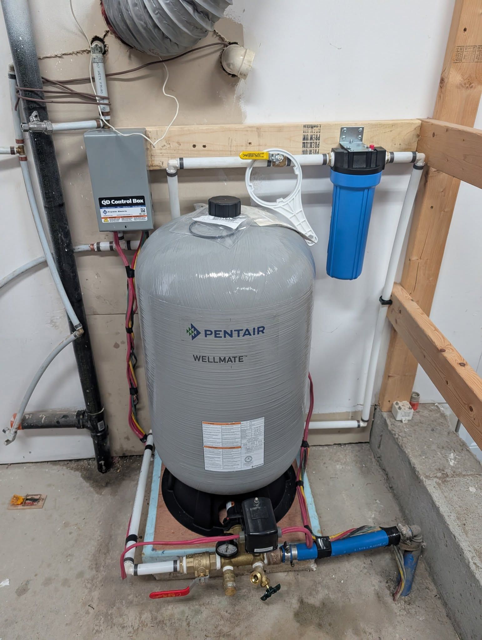 Réservoir d'eau sous pression, filtre et pompe dans un local technique. Réservoir d'eaux grises, filtre à eaux bleues, tuyauterie et boîtier de commande.