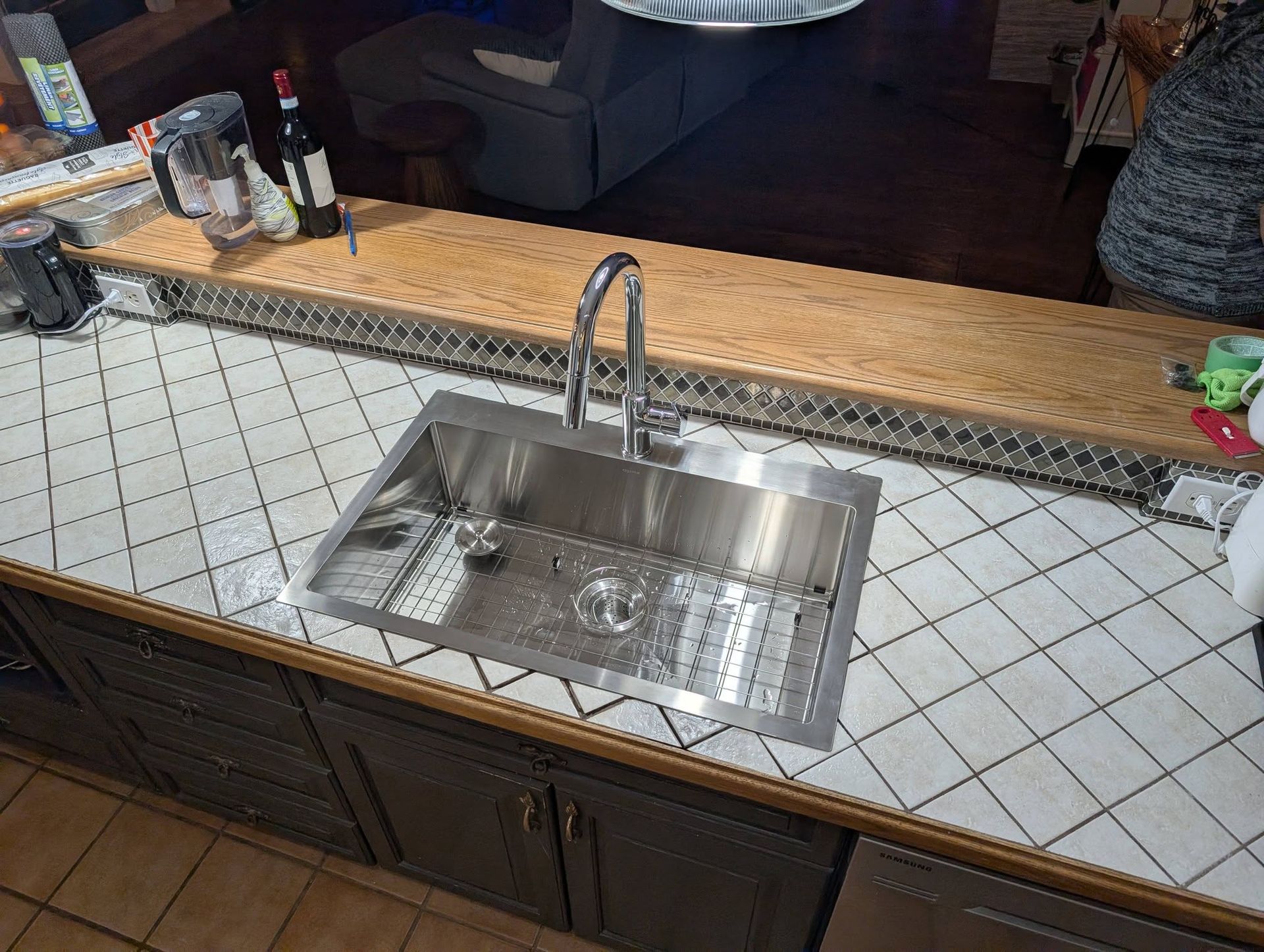Évier de cuisine en acier inoxydable sur un plan de travail carrelé avec des placards foncés.