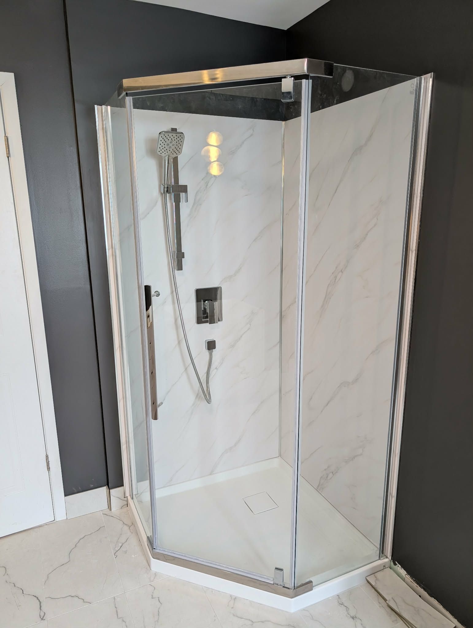 Douche d'angle avec carrelage imitation marbre blanc, robinetterie chromée et portes en verre, dans une salle de bains.