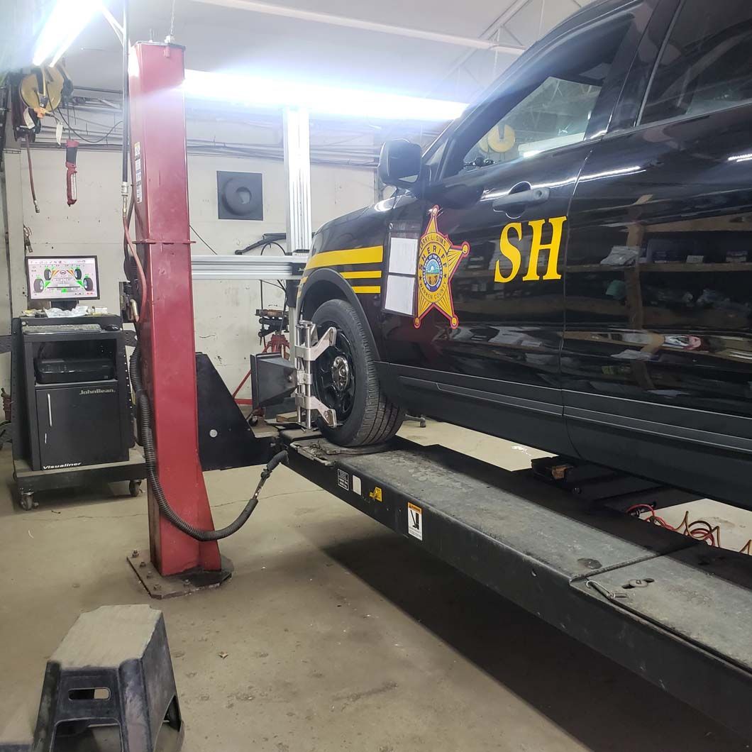 Black sheriff's vehicle on a lift in a garage for an alignment, with yellow and gold details.