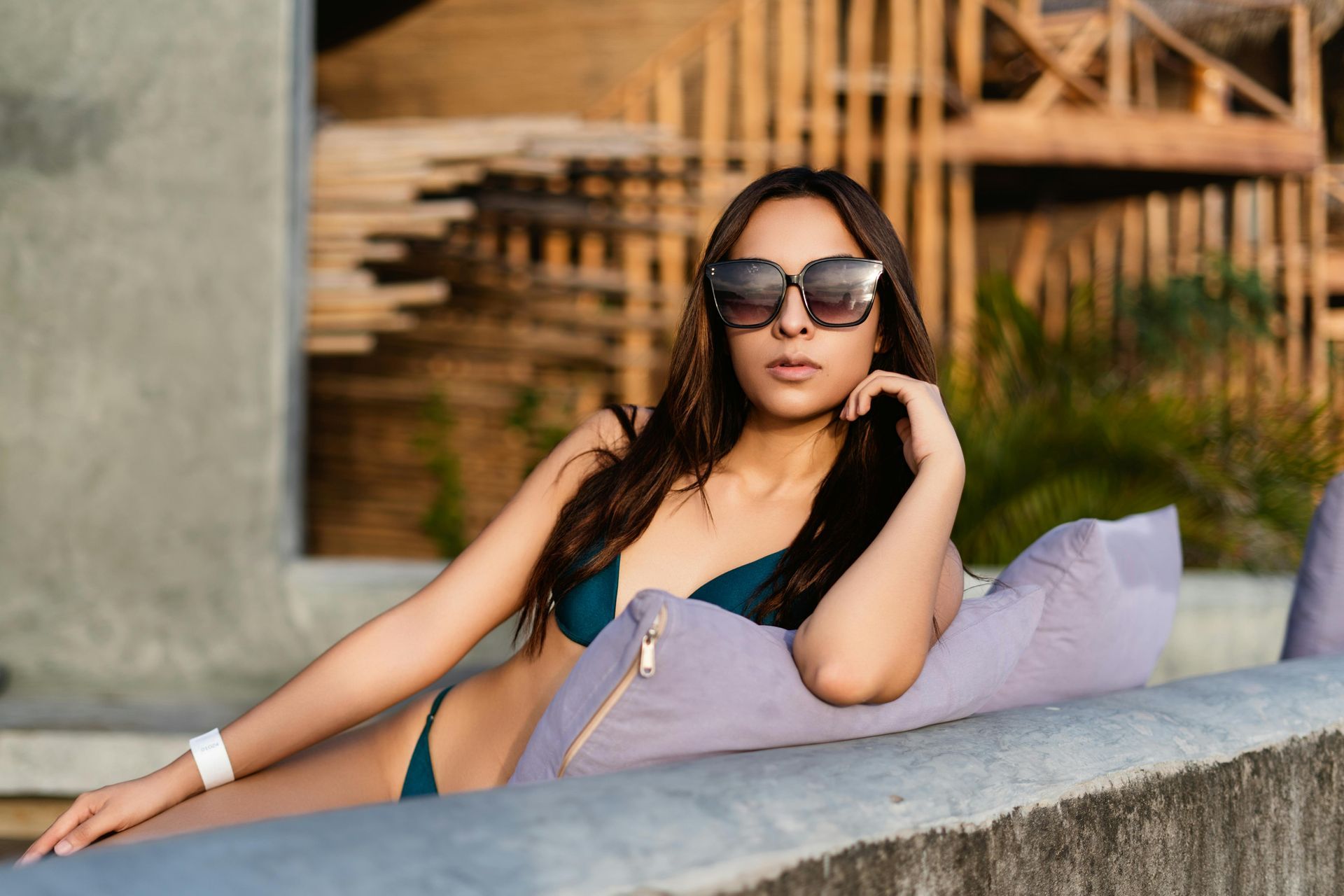 A woman in a bikini and sunglasses is sitting on a couch.