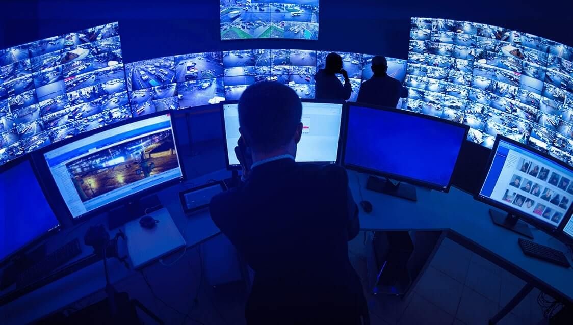 Un uomo è seduto alla scrivania davanti a una serie di monitor.